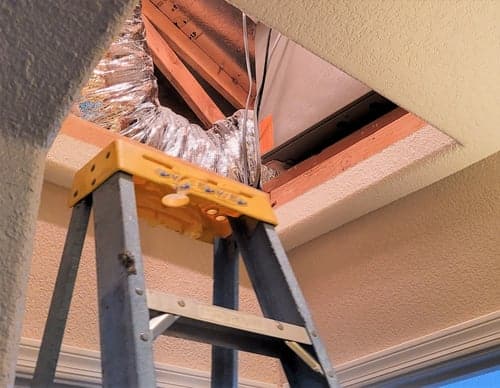HVAC technician installing ceiling ductwork during a residential system upgrade