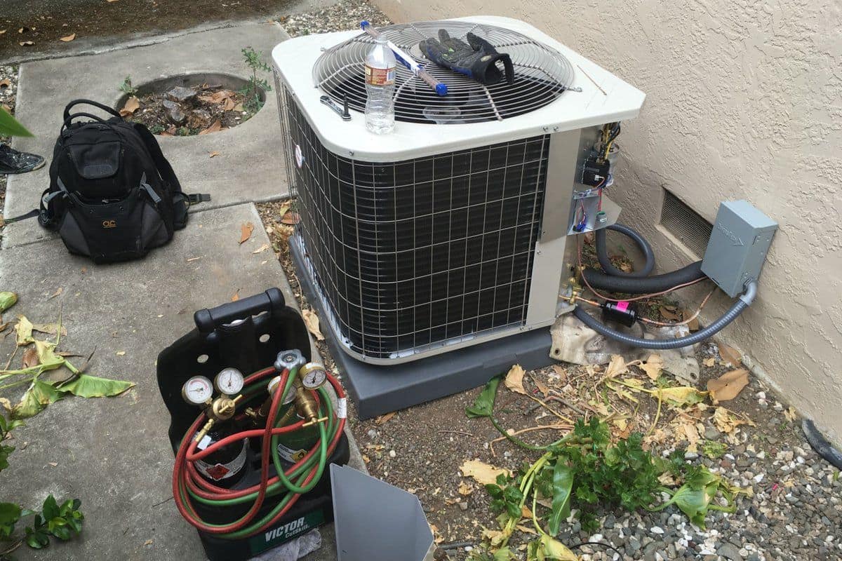 Refrigerant gauges and diagnostic tools set up beside a residential AC condenser during a service call